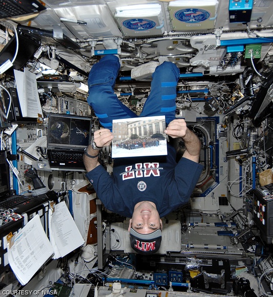 Astronaut Gregory E. Chamitoff PhD ’92 poses with a picture of MIT’s Aeronautics and Astronautics Department aboard the International Space Station during his time in orbit last year.