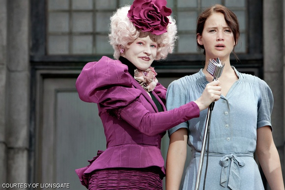 District 12’s rep Effie Trinket (Elizabeth Banks) with a reluctant Katniss Everdeen (Jennifer Lawrence) moments after the Reaping.