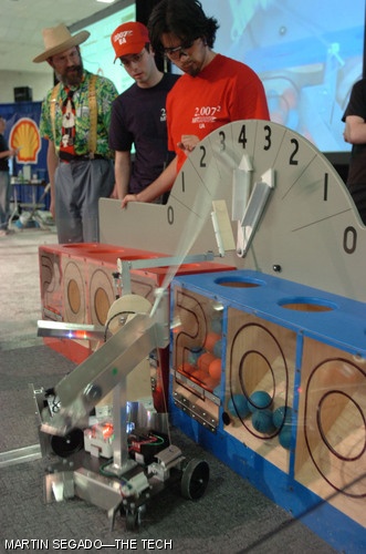 Senior Stephanie A. Sidelko's robot (foreground) and junior Keith M. Molina's robot (partially obscured) fight for control of the score-multiplying arrows on this year's 2.007 contest table while competition staff look on.