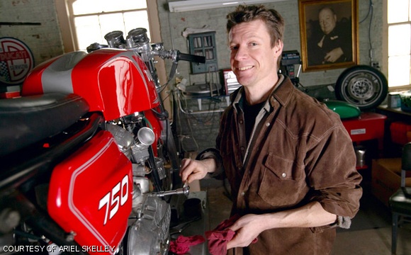 Matthew B. Crawford stands next to a 973 Ducati 750 GT in his motorcycle service shop in Richmond, VA. The portrait on the wall is of Winston Churchill.