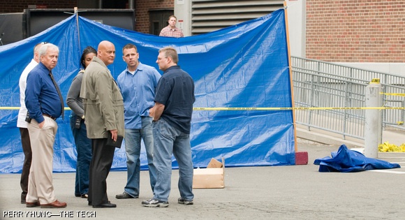 Emergency personnel, including MIT Police Captain Albert F. Pierce Jr. (center, facing right), investigate the death of Han D. Nguyen G, who was found in the parking lot on the east side of Building E19 on Tuesday, June 2. A tarp wall was constructed to shield the location where Nguyen fell (behind tarp to left).