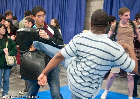 A member of the MIT Sport Taekwondo team holds a pad while a prospective freshman gives it a solid kick.