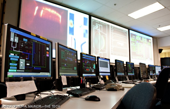 Rows of computer monitors and a massive screen on the rear wall in the control room display crucial data about the tokamak system.