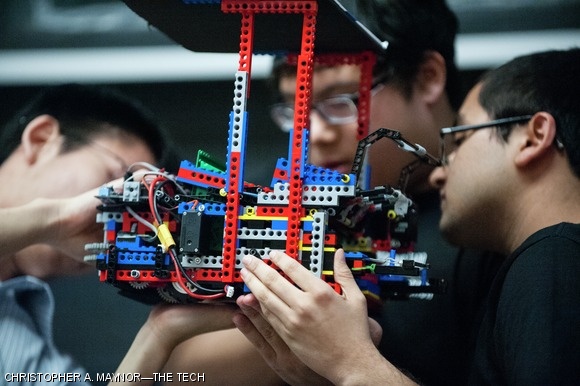 Three teammates examine their robot during the competition.