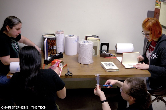 Yelena Tsitkin ’06, Jennifer Chung ’02, D.W. Rowlands G, and Laura A. McKnight ’15 work together to add custom-sized protective covers to the dust-covers of books before they are shelved. The hardcover books had been sitting in boxes until more space could be made.